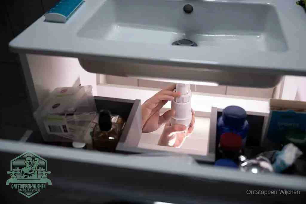 Een pompfles met zeep boven een wastafel, de heet water en afwasmiddel-methode om een vetprop in de afvoer los te maken in Wijchen