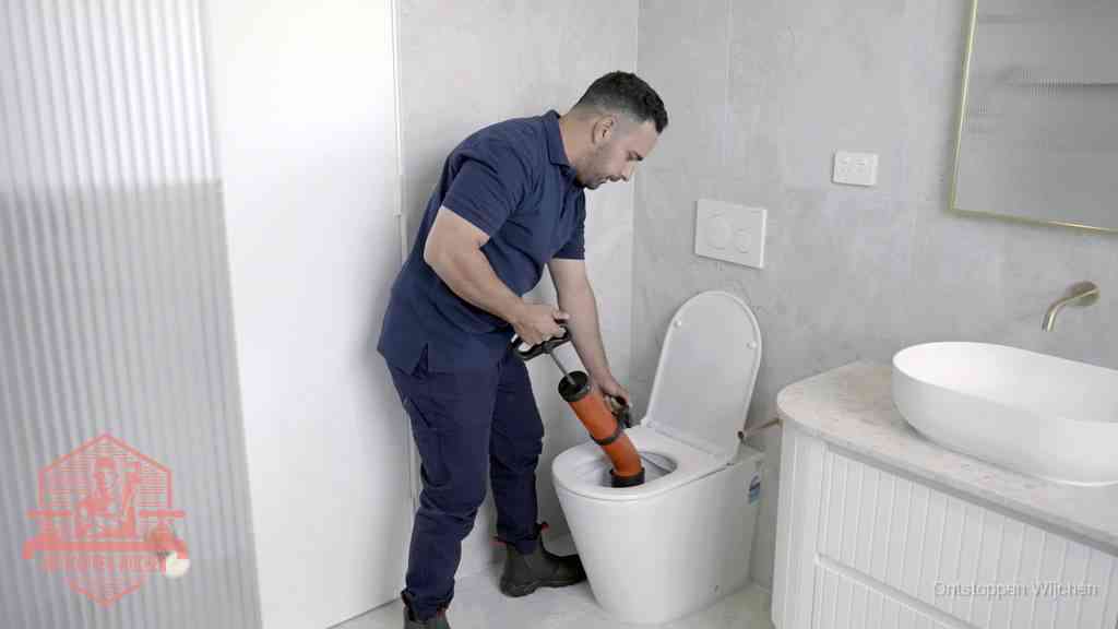 Een monteur buigt over een wandcloset en duwt met de hand een persluchtontstopper in de toiletpot om de verstopping handmatig los te maken in Wijchen