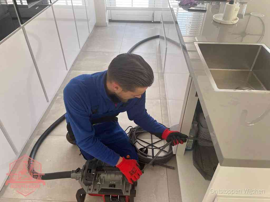 Een monteur ontstopt de keukenafvoer onder de spoelbak met een elektrische veermachine in Wijchen