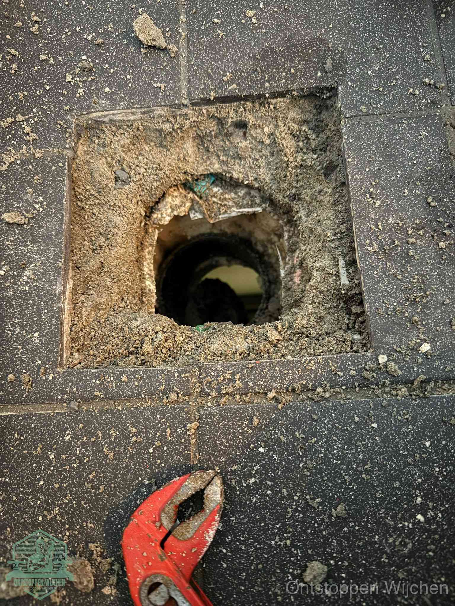 Een geopend rioolputje in een betontegelvloer met losgemaakt rooster en een zichtbare ronde afvoerbuis, het achterhalen waar de afvoerverstopping zit in Wijchen
