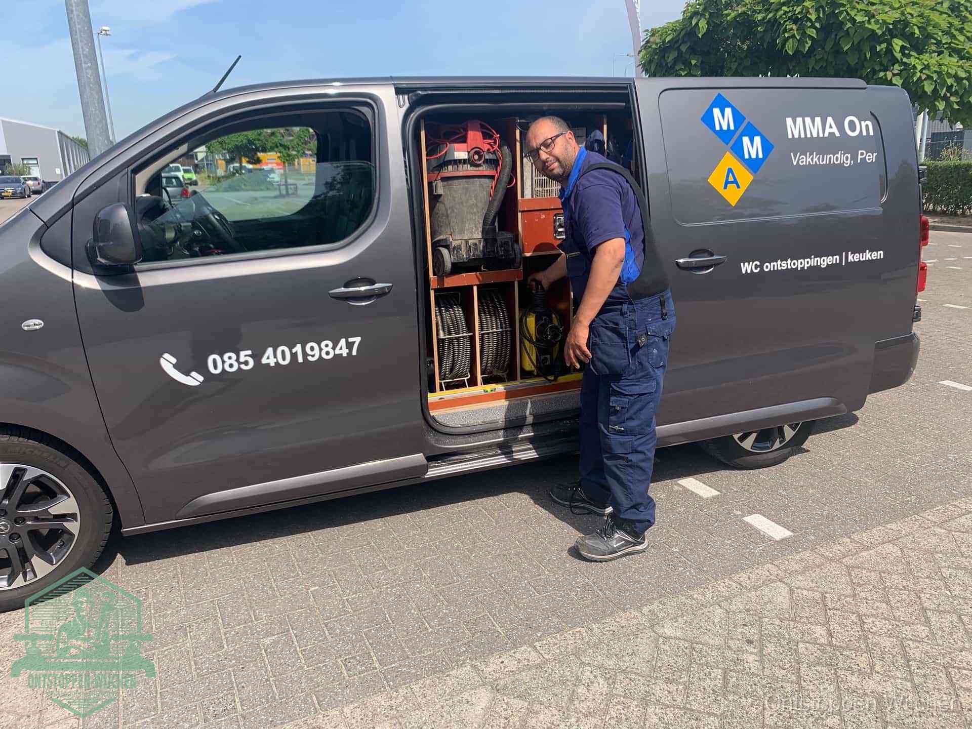 Een monteur bij de open schuifdeur van zijn bedrijfsbus op een parkeerplaats, klaar om de oorzaak van terugkerende afvoerverstoppingen aan te pakken in Wijchen