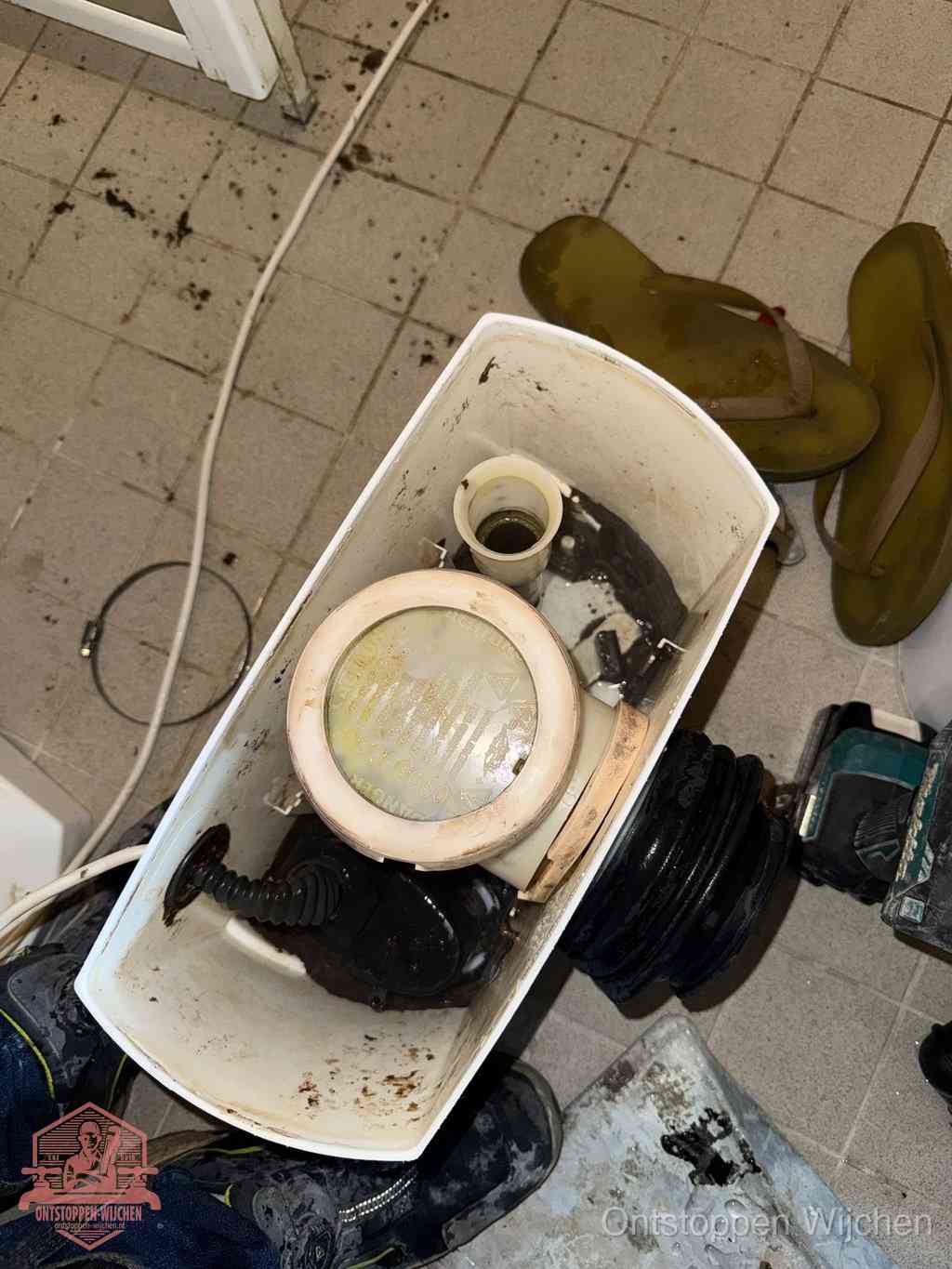 Een gedemonteerde toiletpot op de vloer met ontstoppingsveer en gereedschap ernaast, het verwijderen van een vastzittend voorwerp uit de wc in Wijchen