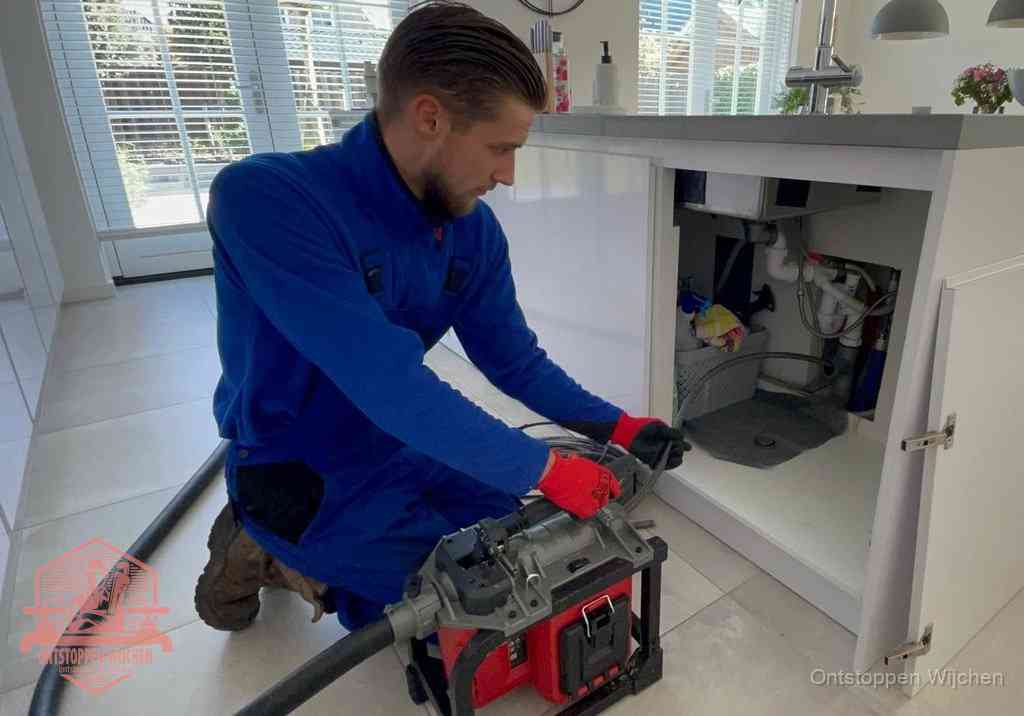 Een monteur voert een professionele elektrische ontstoppingsmachine in de afvoer onder de spoelbak tijdens het gootsteen ontstoppen in Wijchen