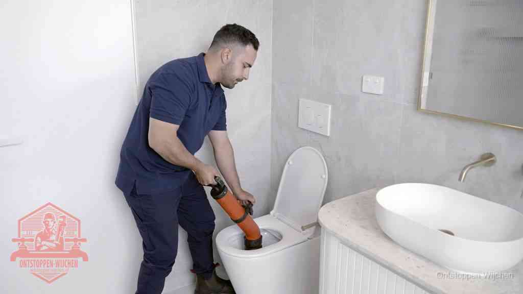 Een man gebruikt een handmatige luchtdruk-ontstopper in een modern betegeld toilet om zelf de wc te ontstoppen in Wijchen